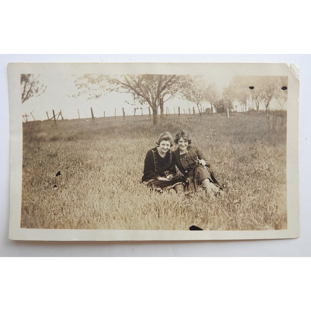 Early 20th century sepia tone snapshot photograph of two young women in a field. Unframed, small corner loss.