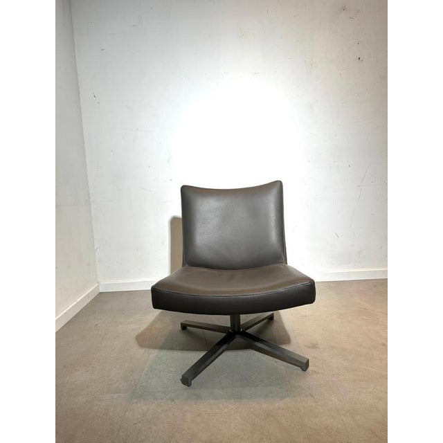 Comfortable modern swivel lounge chair upholstered in brown leather, featuring a clean, minimalist silhouette and a sturdy...