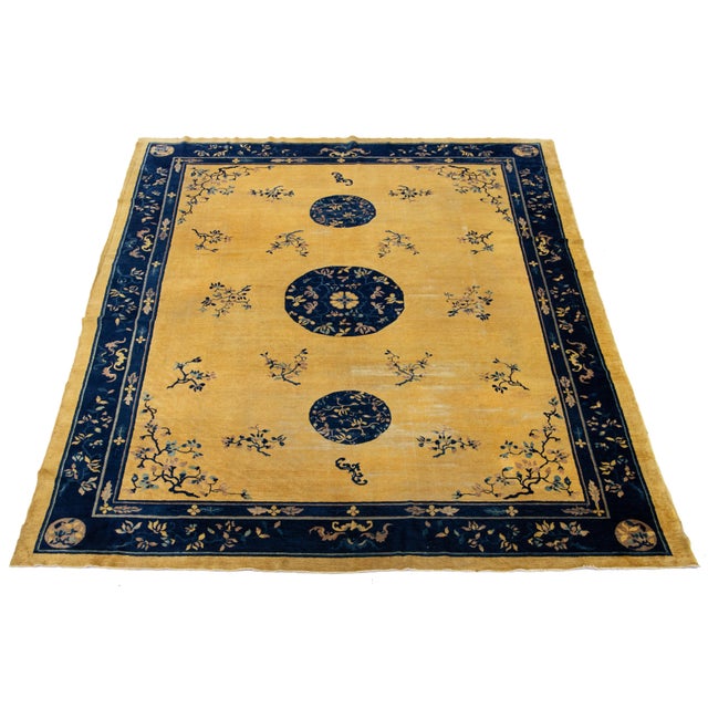 This elegant antique Peking Chinese wool rug features a goldenrod field with a decorative border and navy blue accents,...