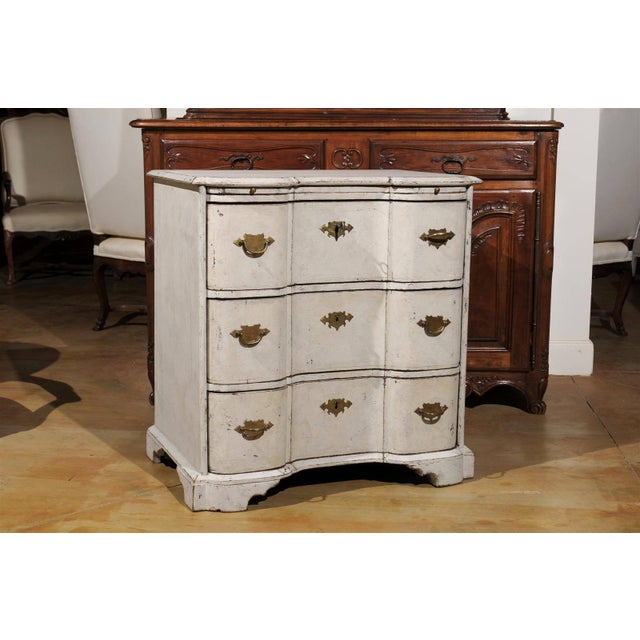 A Danish serpentine front three-drawer painted wood commode from the mid 18th century with pull-out shelf. This three-...