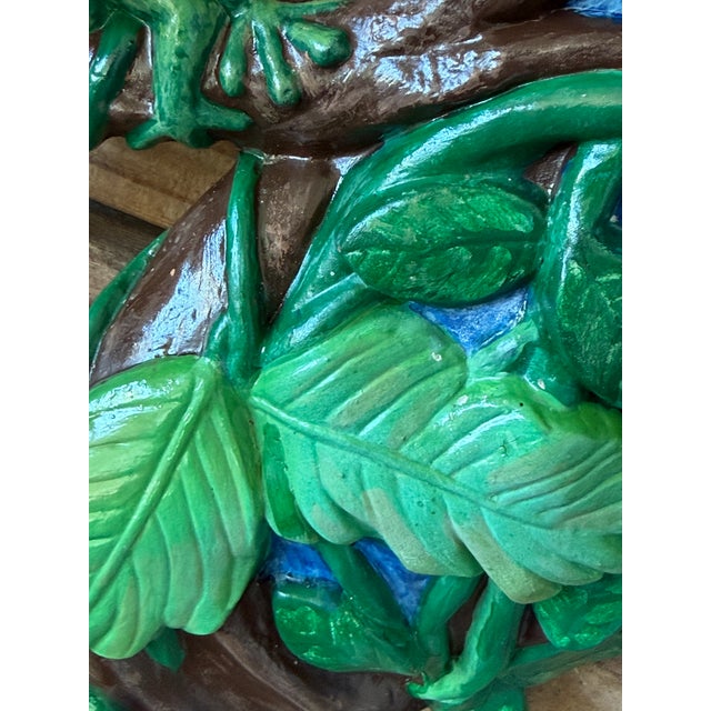 A wonderfully kitschy vintage ceramic wall sculpture featuring colorful tropical birds perched among lush foliage with a...