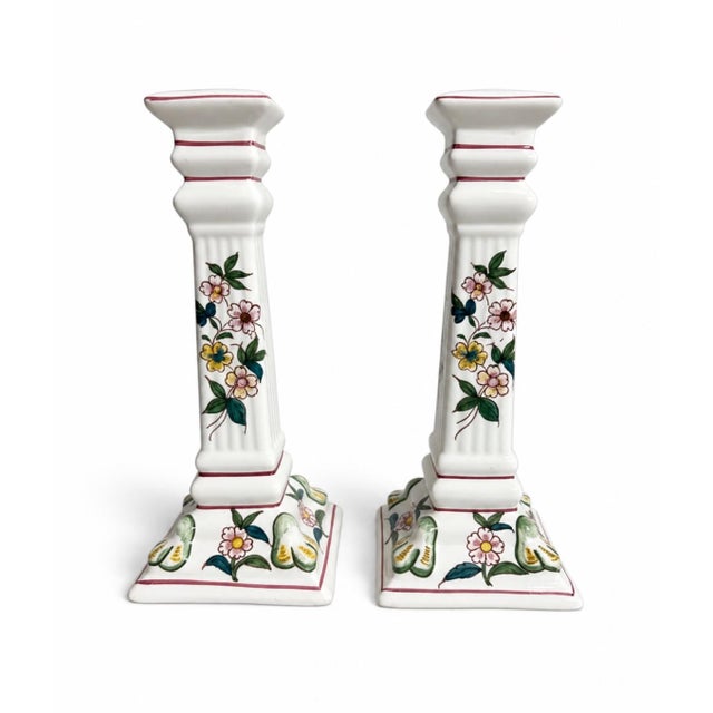 A graceful pair of hand-painted ceramic candlesticks with tall, architectural square-column silhouettes. Each is decorated...