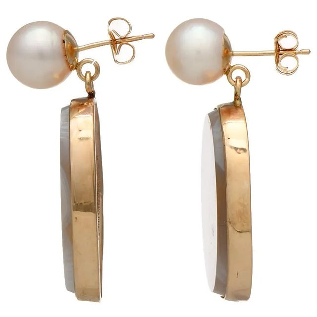 Shimmering agate stuns in the center of these elaborate earrings with yellow gold bases and glittering pearls on top. The...