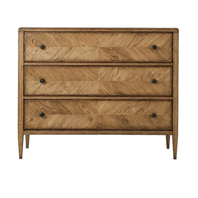 A rustic chest of drawers crafted with light rustic oak. It has a mirrored herringbone oak parquetry design with three...