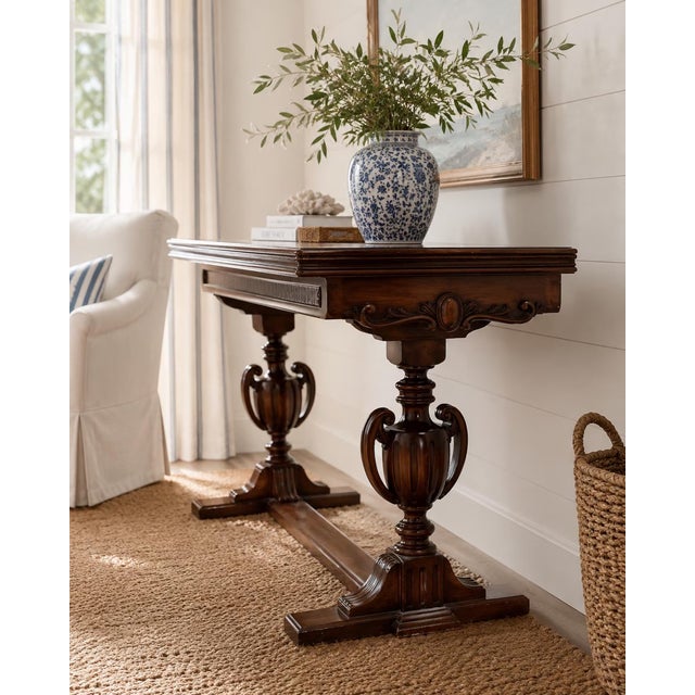 A beautifully carved antique walnut flip-top game table featuring dramatic pedestal urn supports, carved detailing, and a...