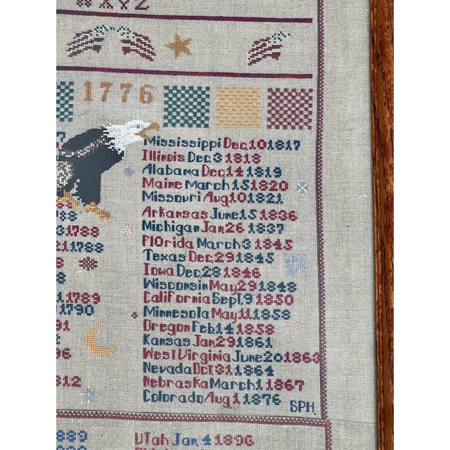 This is a framed, hand-stitched sampler featuring a patriotic American theme, complete with an alphabet, an eagle, the...