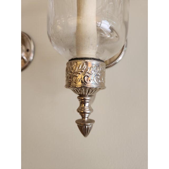 A pair of glass bell shape wall light features a curved nickel finish arm with a single light for E12 bulb.