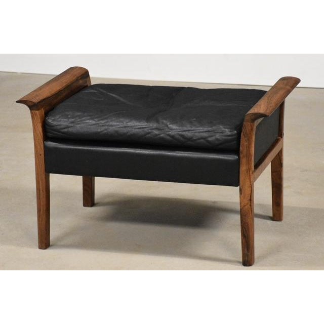 A mid century modern black leather ottoman with rosewood arms designed by Knut Saeter for Vatne Möbler. Beautiful curved...