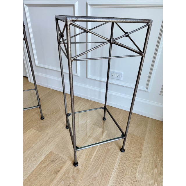 An elegant pair of vintage silvered iron pedestal tables featuring hand-forged construction, inset glass shelves, and...