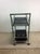 This postmodern bar cart features chrome frame with three bottle holders, rectangular design, black glass shelving on top...