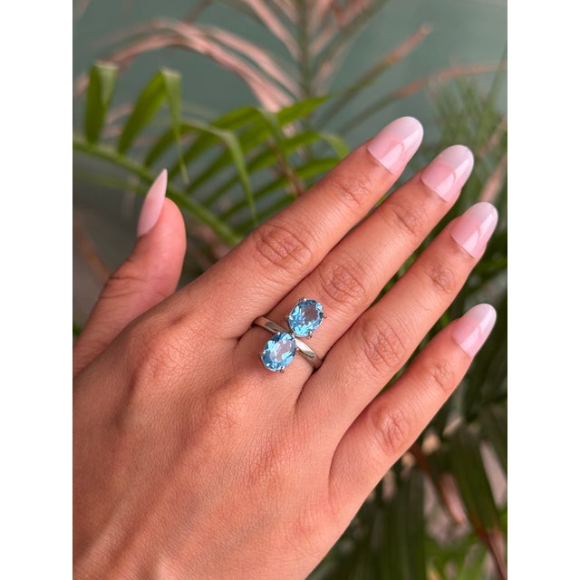 This exquisite ring is beautifully crafted in 925 Sterling Silver, showcasing two oval Blue Topaz gemstones in a refined...