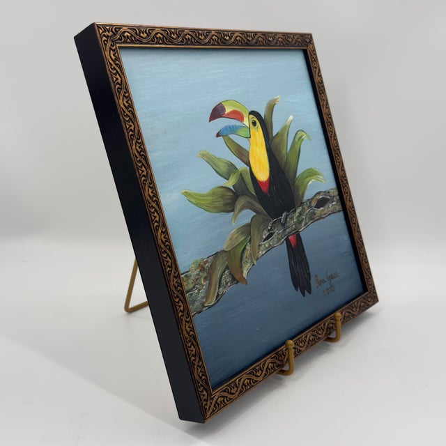 Original painting featuring a colorful toucan perched among lush tropical foliage against a soft blue background. The...