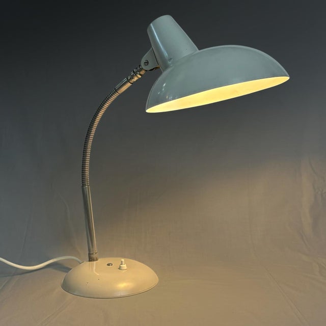 A bauhaus-style table lamp, made from metal with a domed shade, a chrome gooseneck, and a round base fitted with an...