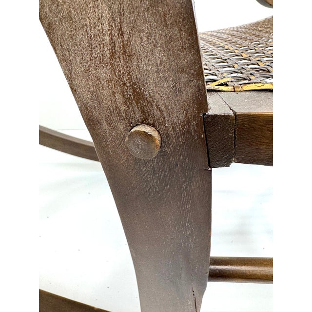 A timeless heirloom, this antique rocking chair features an elegant caned back and seat framed by sculptural scroll arms....