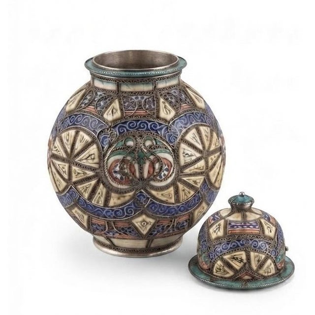 DESIGN & EDITORIAL NARRATIVE This striking Moroccan lidded jar masterfully blends hand-shaped potterywith intricate metal...