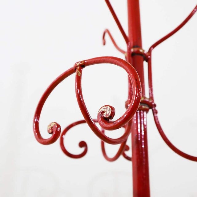 Red metal freestanding coat rack featuring curved hooks.