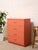 A bold vintage highboy dresser refinished in a saturated burnt orange, giving its clean, streamlined silhouette a fresh...