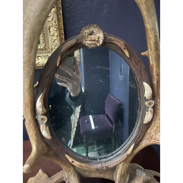 An antique antler vanity mirror with an antler base and larger antlers flanking a small carved wooden oval mirror frame-...