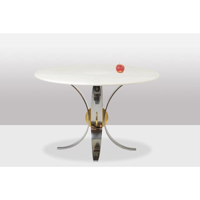 Dining room table, or pedestal table, round in shape. White marble top resting on a saber-shaped chrome and gold metal...