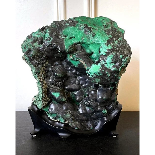 A natural malachite rock specimen with striking green and black colors fitted on a wood stand for viewing and meditating....