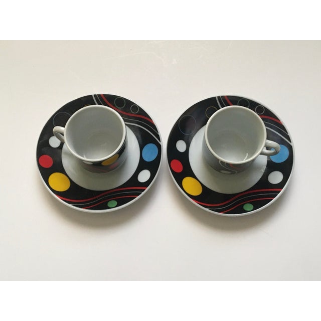 A pair of geometric expresso mugs with a pattern of circles and wavy lines in yellow, red, blue, black & white. Saucers...