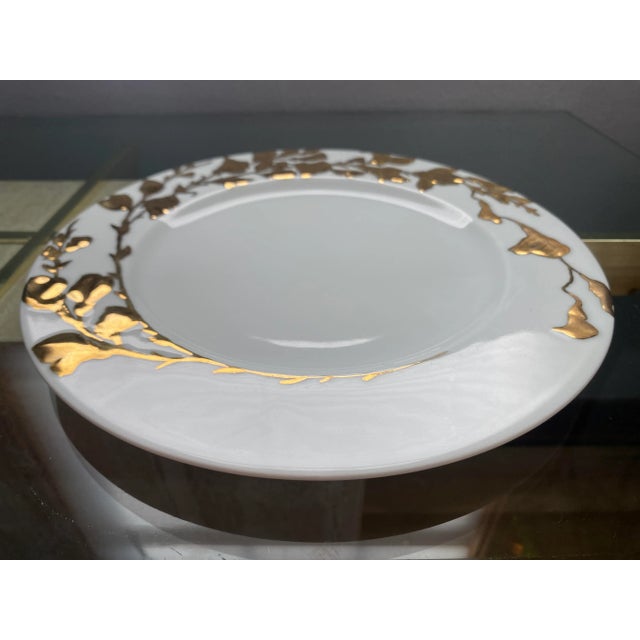 A delicate white porcelain dinner plate adorned with hand-painted gold flowers, by Philippe Deshoulieres for De Limoges...