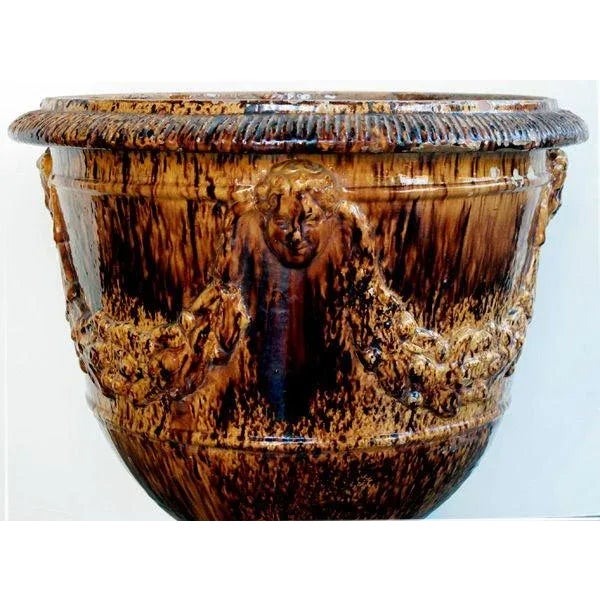 A handsome French brown-glazed anduze pot; the gadroon lip above a cup-shaped bowl adorned with 4 masks joined by plump...