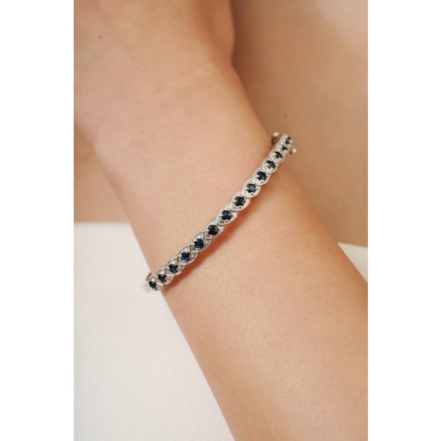 This elegant sterling silver sapphire bangle bracelet showcases a refined row of deep blue sapphires set in a delicate...