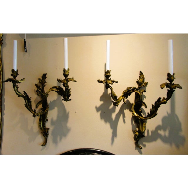 This antique pair of French 19th century Louis XV gilt bronze two light wall sconces exudes elegance and sophistication....