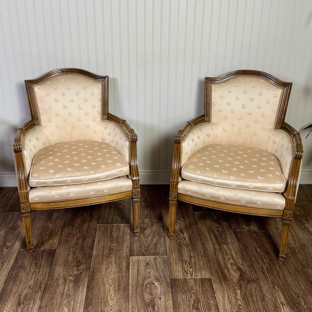 This mid-century vintage pair of Directoire-style bergère armchairs features a wood frame (possibly walnut or fruitwood)...