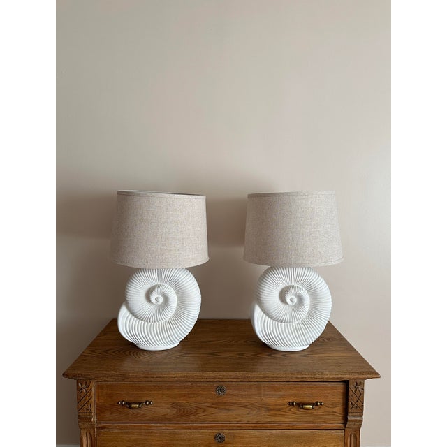 A pair of table lamps formed in a spiral shell shape, constructed from plaster with a matte white finish and ribbed...