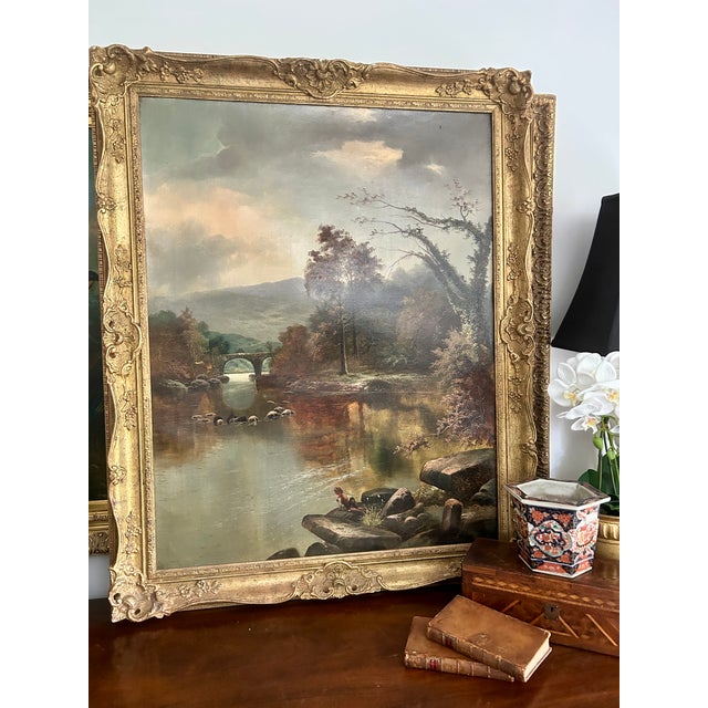 A handsome 19th-century oil on canvas depicting an atmospheric river landscape with a stone bridge, wooded banks, distant...