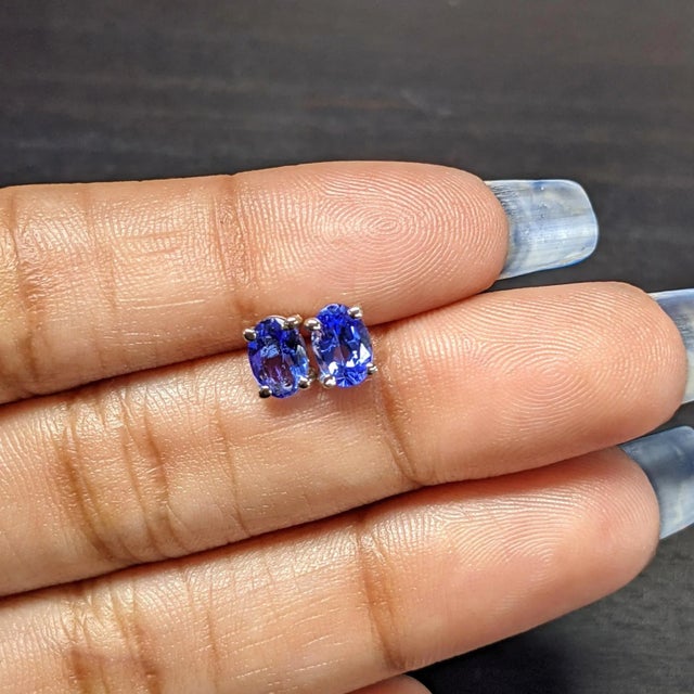These elegant earrings feature oval tanzanite gemstones, exuding a captivating violet-blue hue. The stones are securely...
