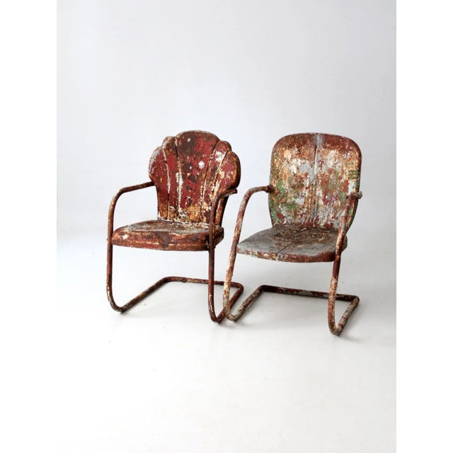 This is a pair of mid-century metal patio chairs. Marvelously aged, the chippy paint metal lawn chairs are a mis-matched...