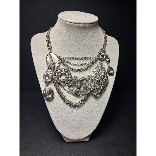 This statement necklace features an antique silver-tone finish with layered chains and assorted charms, including a leaf,...