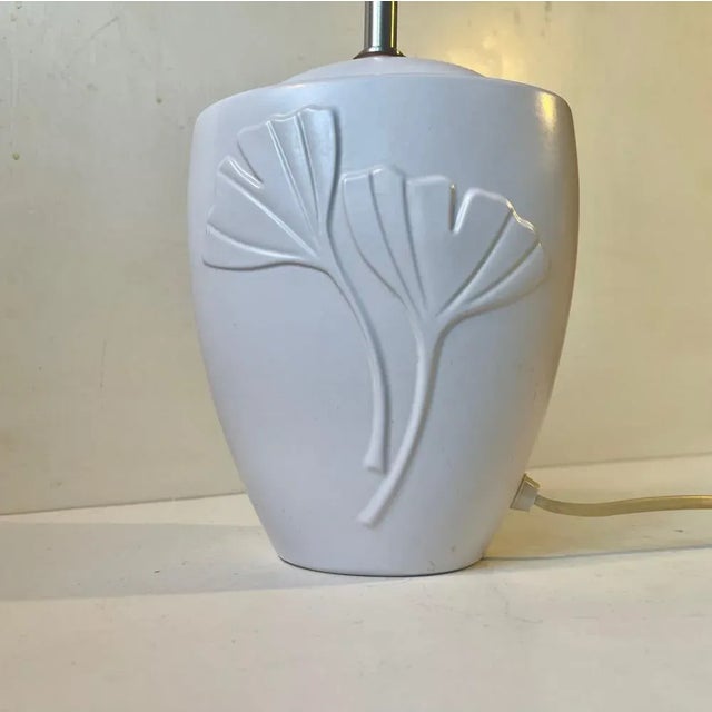 A white glazed table light featuring stylized relief flowers and fluted white shade. Art deco revival in style. Made at...