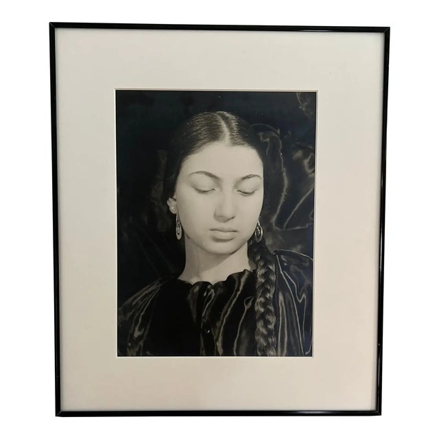 A large vintage black and white photograph of a young girl with long dark hair styled in a center part and a single braid...