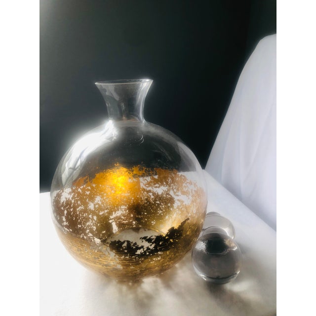 Mid-century modern clear glass decanter featuring a hand-applied gilt gold interior band. The spherical stopper and...