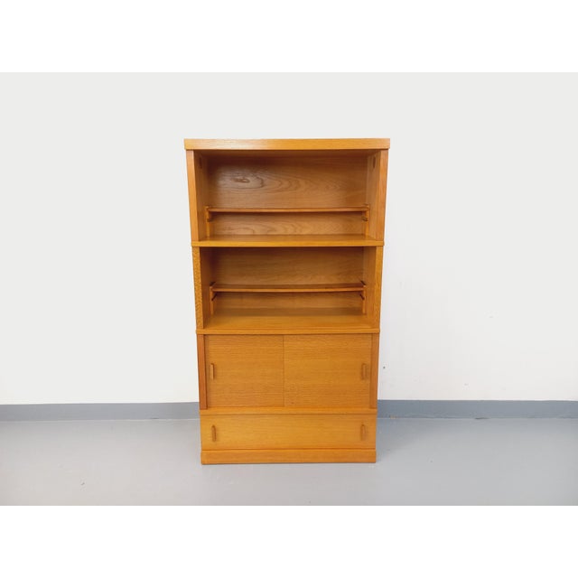 Vintage 1960s oak bookcase with a solid plinth, two open shelves with small removable shelves, two sliding doors, and one...