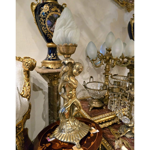 Elegant French Rococo style table lamp featuring a beautifully sculpted cherub figure holding an ornate torch-style light...