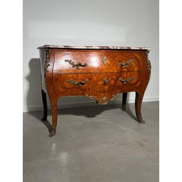 Elegant antique bombe chest of drawers featuring exceptional marquetry inlay work and a striking marble top. A refined...