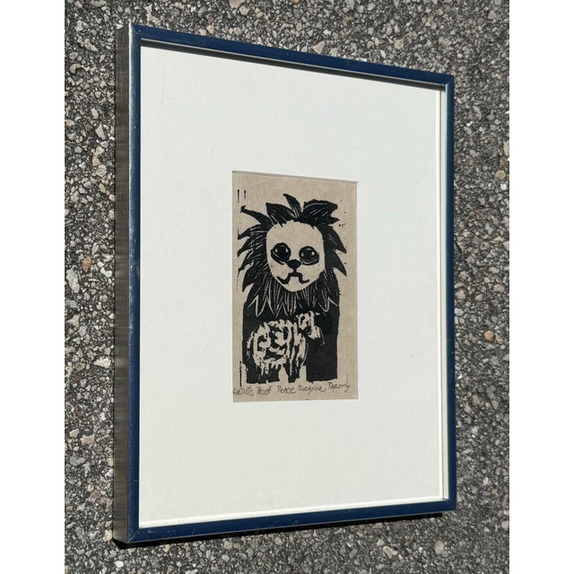 A charming and slightly surreal piece, this black-and-white linocut print features a wide-eyed lion with a human-like face...