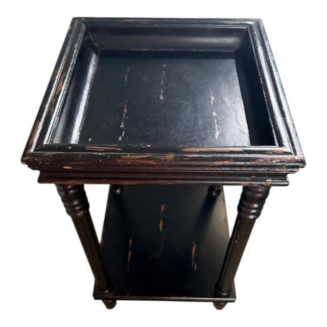 Charming vintage two-tier side table featuring a rich black painted finish with beautifully aged, naturally distressed...