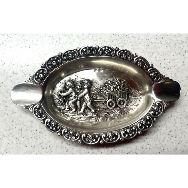 This antique German 800 Repousse silver ash tray is a rare find, featuring a scene with cherubs pulling a flower cart with...