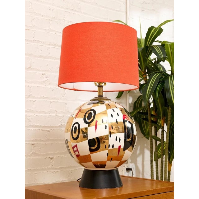 bold postmodern table lamp pairing a sculptural rounded ceramic base with a vivid red fabric drum shade. The glossy base...