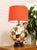 bold postmodern table lamp pairing a sculptural rounded ceramic base with a vivid red fabric drum shade. The glossy base...