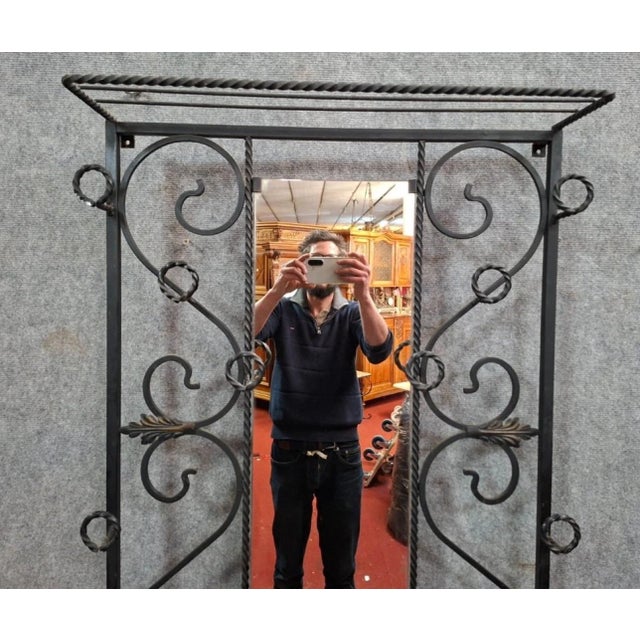 Elegant wrought iron wall-mounted coat rack, featuring a central mirror and a richly detailed design of scrolls and spiral...