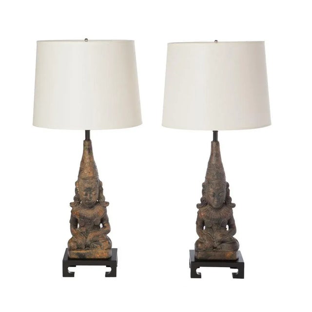 Pair of 1950s gilt metal Asian seated figural lamps on black ebonized platform bases, in the style of James Mont.