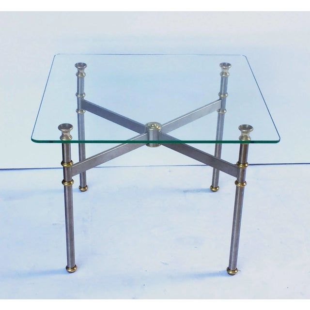 A fine French low table featuring a square clear glass top set upon a stylish base of brushed steel and brass. Perfect for...