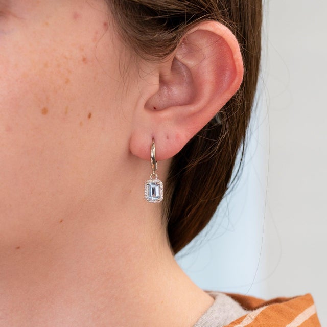 Serene aquamarines rest within a sparkling diamond halo in these emerald-cut studs, set in solid 14K white gold. Their...